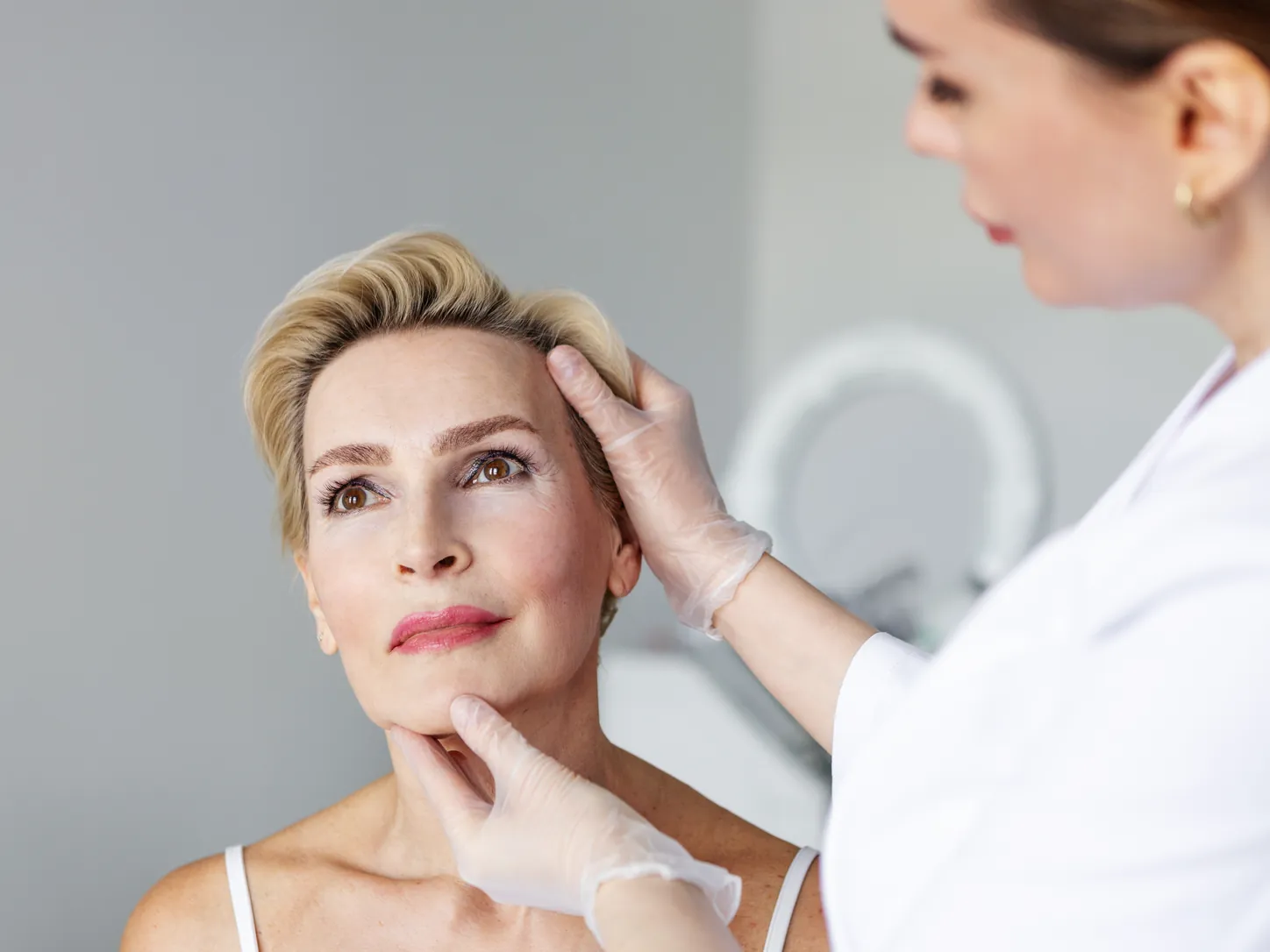 Profesional sanitaria valora el rostro de una paciente antes de un tratamiento estético